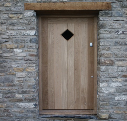 Ledged oak front door with a diamond window in a stone wall
