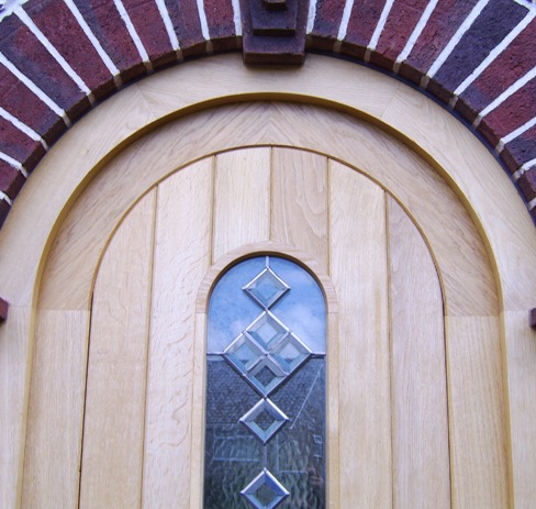 Arched oak front door with leaded glass set in a brick arch