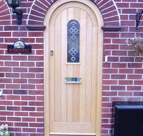 Arched oak front door with a leaded window in a brick house