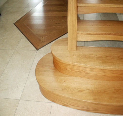 Rounded oak bottom steps on a tiled floor with an inlaid border