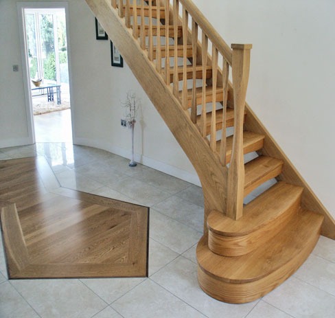 Curved oak staircase rising from a tiled hall with an inlaid timber floor