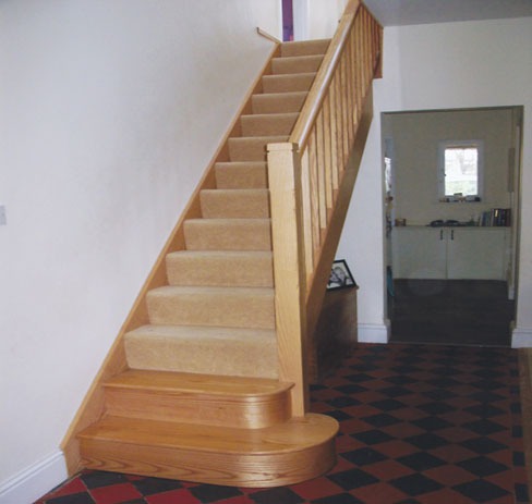 Carpeted oak staircase with a curved bottom step
