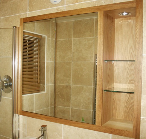 Oak framed recessed mirror and shelving in a tiled bathroom